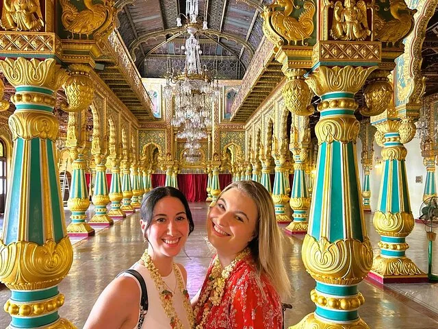 Zwei lächelnde Frauen in der kunstvollen, farbenfrohen Durbar Hall des Mysore-Palastes.